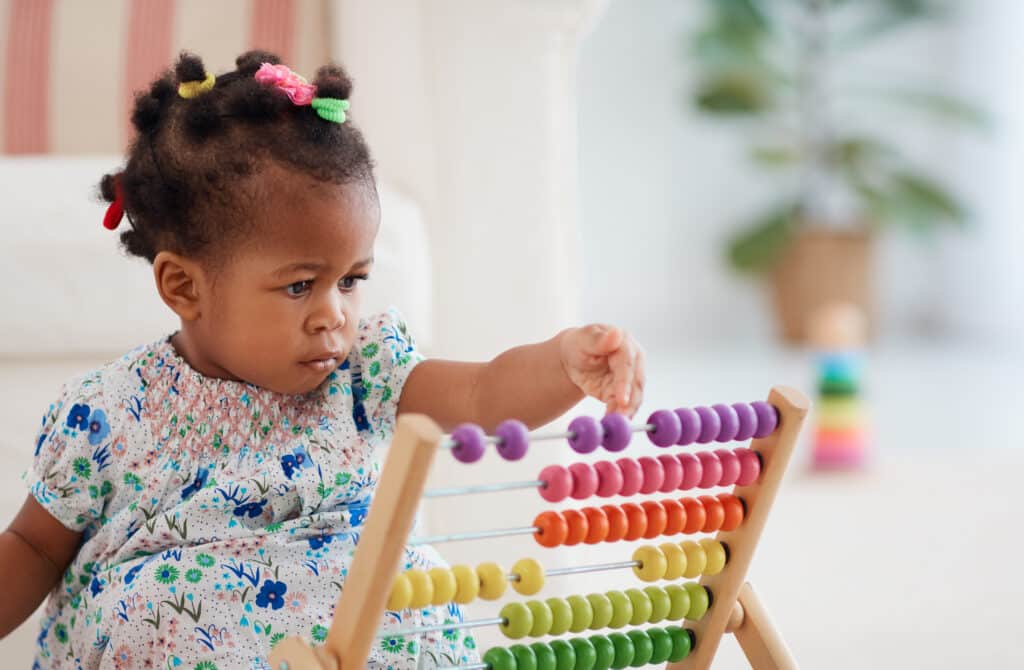 Enfant joue avec boulier coloré apprentissage Jeune enfant métisse concentrée jouant avec un boulier en bois coloré à perles violettes, roses, oranges, jaunes et vertes.