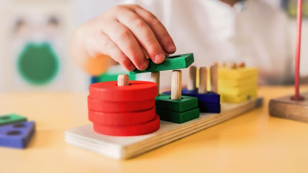 Main d'enfant manipulant un jeu d'éveil en bois coloré pour développer sa motricité fine et l'apprentissage.